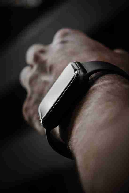 A detailed close-up of a smartwatch on a person's wrist, highlighting the sleek design and reflective screen of the device. The angle captures the curvature of the wrist, with a hint of the person's chin in the background, set against a soft-focus backdrop that accentuates the smartwatch as the central subject of the image.
